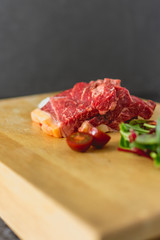 Slices of fresh raw beef steak on wooden board on black background with salad and tomatoes