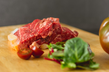 Slices of fresh raw beef steak on wooden board on black background with salad and tomatoes
