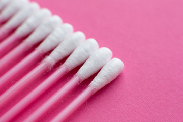 Closeup view from above on cotton buds laid in a diagonal line on pink background