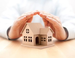 Property insurance. House miniature covered by hands. 