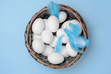 White Eggs in a Wicker Basket with Feathers on Textured Paper Background. One of the Easter Symbols.