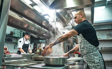 How to cook a meat Concentrated young chef in apron and cooks preparing food together in a restaurant kitchen