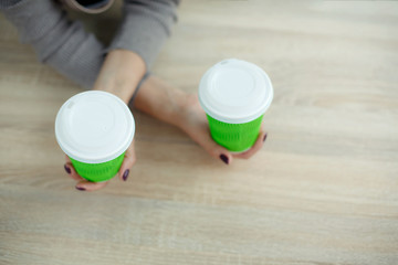 Barista in apron is holding in hands hot coffee in green takeaway paper cup. Coffee take away at cafe shop