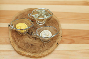 Obraz na płótnie Canvas Set of three transparent sauceboats with different sauces on wooden plate