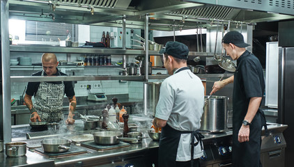Cooking process. Professional team of chef and two young assistant preparing food in a restaurant kitchen