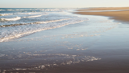 A tranquil scene of the beach at Bamburgh, Northumberland, with sand and a stream flowing towards the sea.
