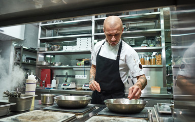 Confidence in everything. Serious male chef with several tattoos on his arms frying ingredients for...