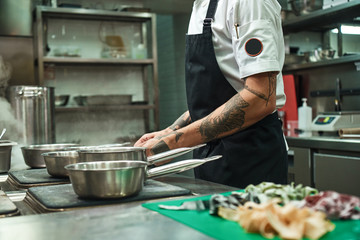 I love Italian food Side view of young chef's hands with tattoos cooking homemade italian pasta in a restaurant kitchen