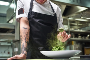 Slow motion. Cropped image of chef's hands with tattoos adding spices in salad while standing in a...