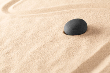 Fototapeta na wymiar Black basalt zen meditation stone in a Japanese sand garden. Minimalism to focus concentration on spiritual healing. An alternative therapy in spa wellness resort. Sand background with copy space.