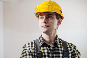 Portrait of a young male builder and repairman in a yellow helmet against the background of a wall.