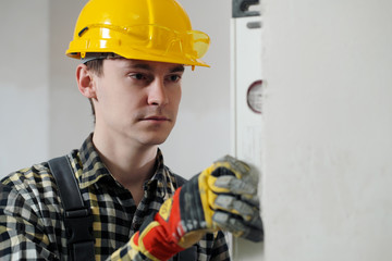 Portrait of a young male builder and repairman in a yellow helmet with level.