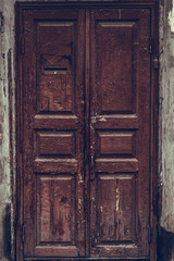 Peeling brown wooden door. Dilapidated wooden grunge door with cracked maroon paint. Threadbare dark red door.