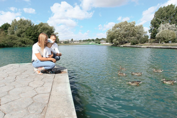 young family feeds wild ducks sitting on a pier by the lake