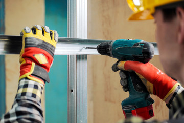 Young male construction worker and repairman working with a screwdriver and metal profile.