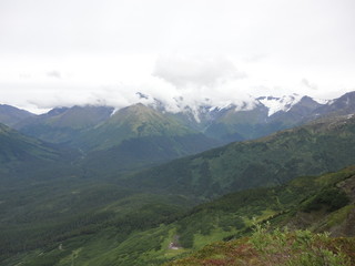 View from atop a mountain in the wilderness of Alaska. Peaks and ocean stretching off into the sky and clouds