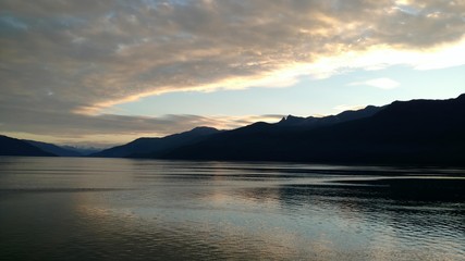 Sunset over the Pacific Ocean setting below a mountain range with bright colors gleaming off the clouds and ocean