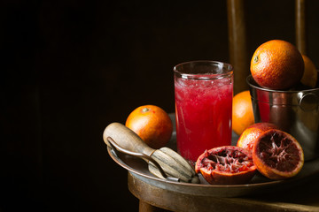 Glass of blood orange juice with ice and orange fruits on dark background