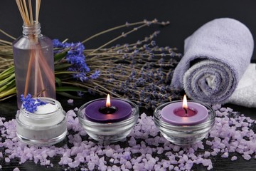Obraz na płótnie Canvas Burning aromatic candles, dry lavender, cosmetics on a black wooden table. Spa and aromatherapy accessories