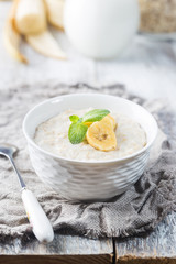 Bowl of oatmeal porridge with banana on white wooden rustic table, healthy breakfast, diet food.