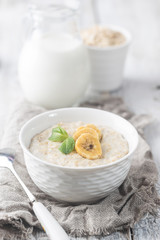 Bowl of oatmeal porridge with banana on white wooden rustic table, healthy breakfast, diet food.