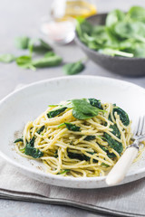 Spaghetti pasta with spinach and green pesto, in a white plate on gray stone background