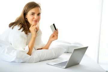 Woman using laptop for store online shopping in bed at home, payment by credit card with online transaction banking with security protection, trusting business finance technology.........