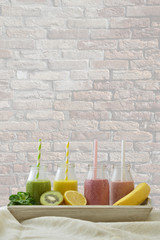 four colorful fruit smoothies in a row with fresh fruits in front of a brick wall with copy space above for a healthy lifestyle