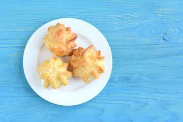Delicious homemade gluten free eclairs on white plate on blue wooden textured table. Tasty french profiteroles filled traditional custard cream. Dish with gourmet pastries on blue wood backdrop 