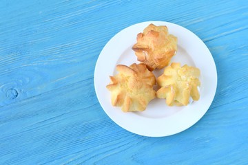 Delicious homemade gluten free eclairs on white plate on blue wooden textured table. Tasty french profiteroles filled traditional custard cream. Dish with gourmet pastries on blue wood backdrop 