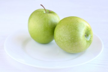 Fresh organic green juicy apples on white plate with selective focus on neutral background. Diet concept with raw vegetarian food. Green apple fruit at the dish