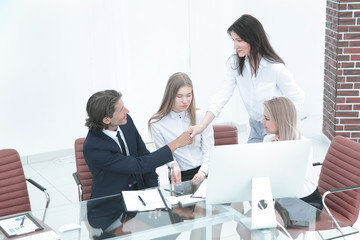 Friendly smiling businessman and businesswoman handshaking over the office desk