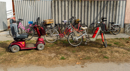 Different Bicycles parked near to fence with gray paint on a street of old village. Old Fashion transportation and  healthy lifestyle.
