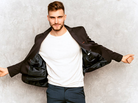 Portrait of handsome serious hipster lumbersexual businessman model wearing casual black suit. Fashion stylish man posing against gray wall