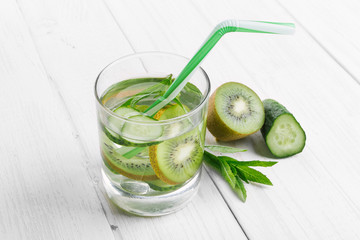 Refreshing drink for detoxification, mineral water in a glass, fresh green kiwi, mint and cucumber on a white table.