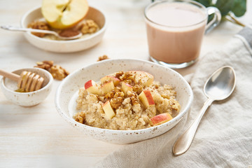 Oatmeal with apple, walnuts and cup of cocoa on white wooden light background. Side view. Healthy...