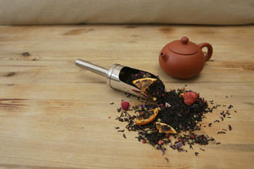 Black tea with pieces of dried berries with a clay teapot on the wooden background with copy space...