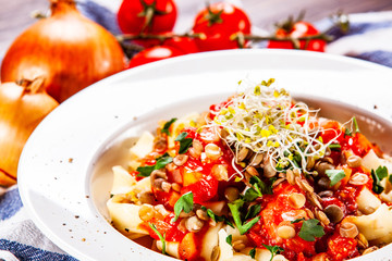 Pasta with tomato sauce and vegetables on wooden table