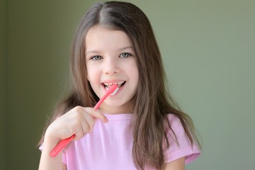 Caucasian beautiful girl brushing her teeth. Long haired smiling white girl brushing teeth with pink toothbrush on green background. Green eyed cute child in pink tshirt doing her morning hygiene. 