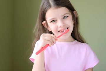 Caucasian beautiful girl brushing her teeth. Long haired smiling white girl brushing teeth with pink toothbrush on green background. Green eyed cute child in pink tshirt doing her morning hygiene. 