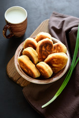 Fried patties or pies filled green onion and eggs on dark wooden background. Pirozhki Russian tradition food.