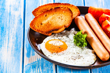 English breakfast - fried egg, sausages, toasts and vegetables