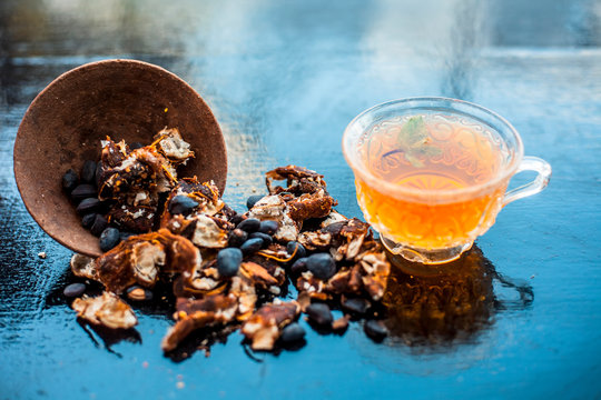Tamarind or imli or amli in a clay bowl along with its roasted seeds and extract tea in a transparent glass cup with mint or mentha leaves on top on wooden surface.