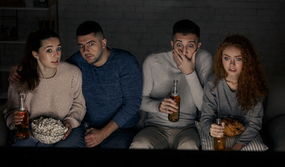 Scared friends watching horror film and drinking beers
