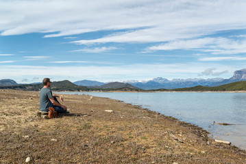 hombre joven sentado a la orilla de un lago, disfrutando del paisaje en un día primaveral.