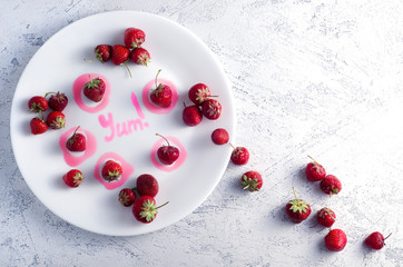 strawberries on a white plate and yum word written with jam. Creative summer image