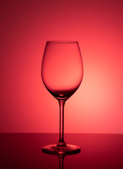 Empty glass on acrylic glass, on red and pink background