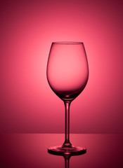 Empty glass on acrylic glass, on red and pink background