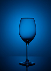 Empty wine glass stands on acrylic glass on a red and pink background.