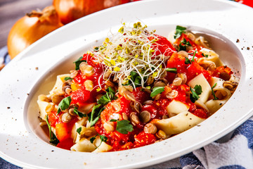 Pasta with tomato sauce and vegetables on wooden table